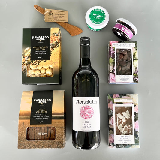 A flatlay gift hamper with wine, chocolate, wooden server, gourmet pastes, crackers and popcorn