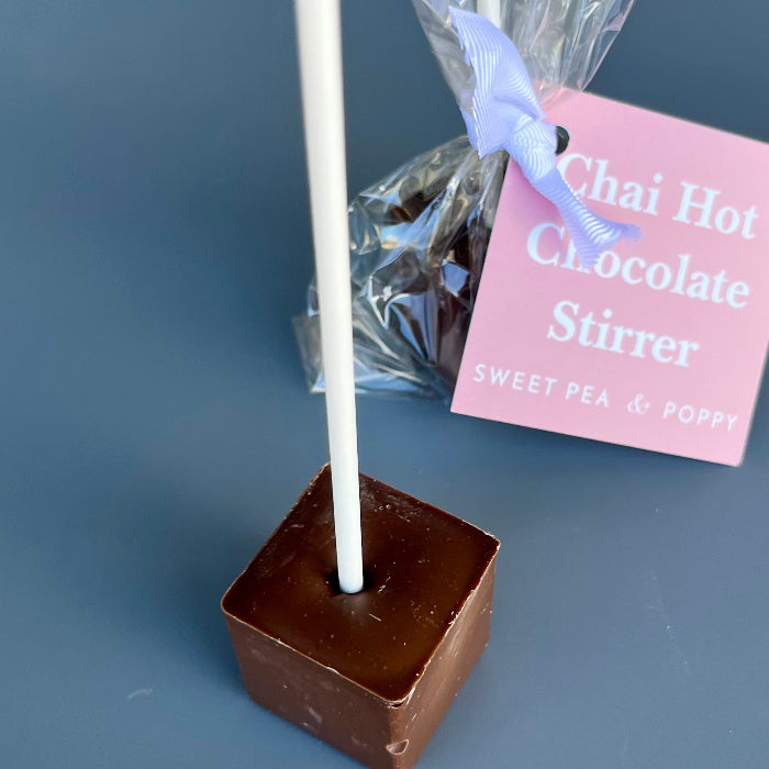 Chocolate-covered hot chocolate stirrer stick with a white handle on a gray background, accompanied by a 'Chai Hot Chocolate Stirrer' packaging.
