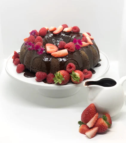 A chocolate cake on a platter topped with berries and ganache