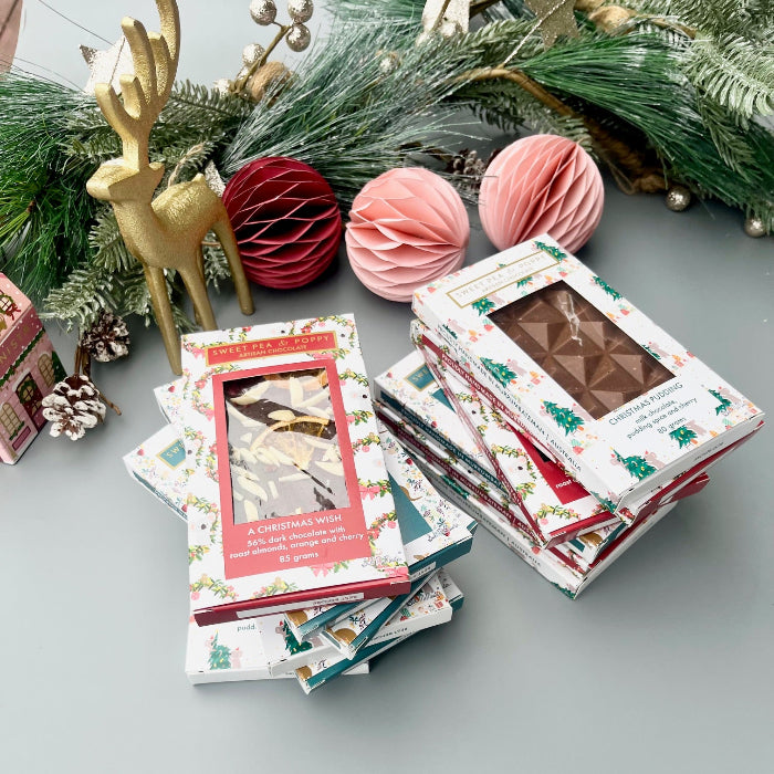 Stack of Christmas-themed chocolate bars on a gray surface with decorative items in the background.