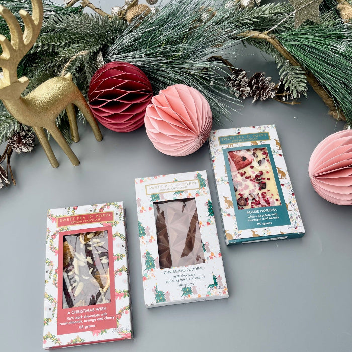 Three chocolate bars with Christmas-themed covers on a gray surface with decorative elements.