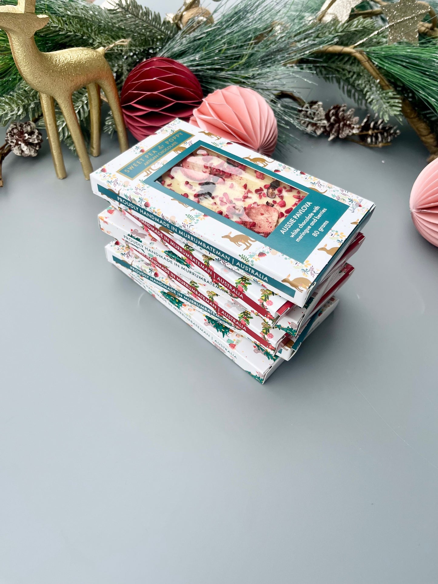 Stack of artisan chocolate bars with Christmas-themed covers on a light gray surface, surrounded by festive decorations.