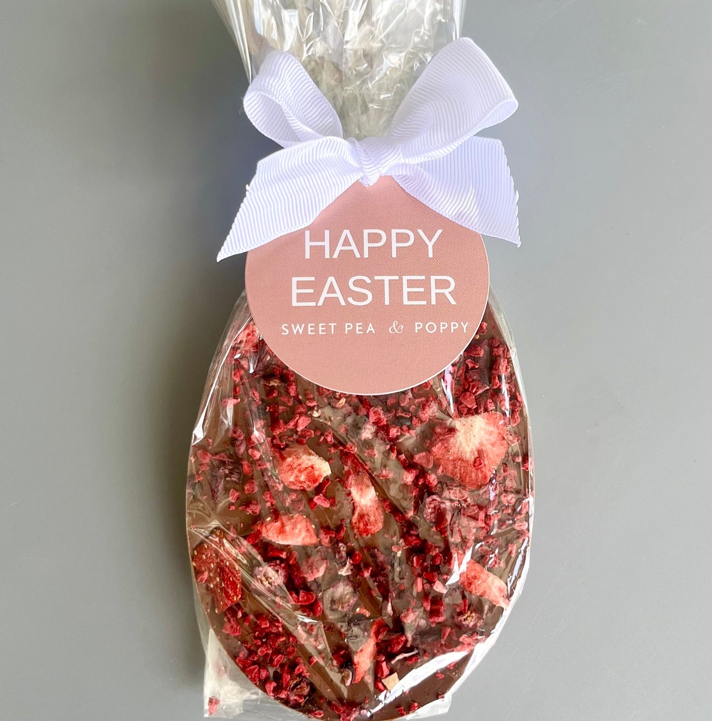 Easter egg shaped chocolate bar in a cello bag with a 'Happy Easter' label on a grey background.