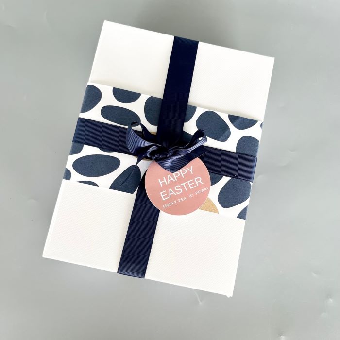 Gift box with navy polka dot ribbon and 'Happy Easter' tag on a gray background