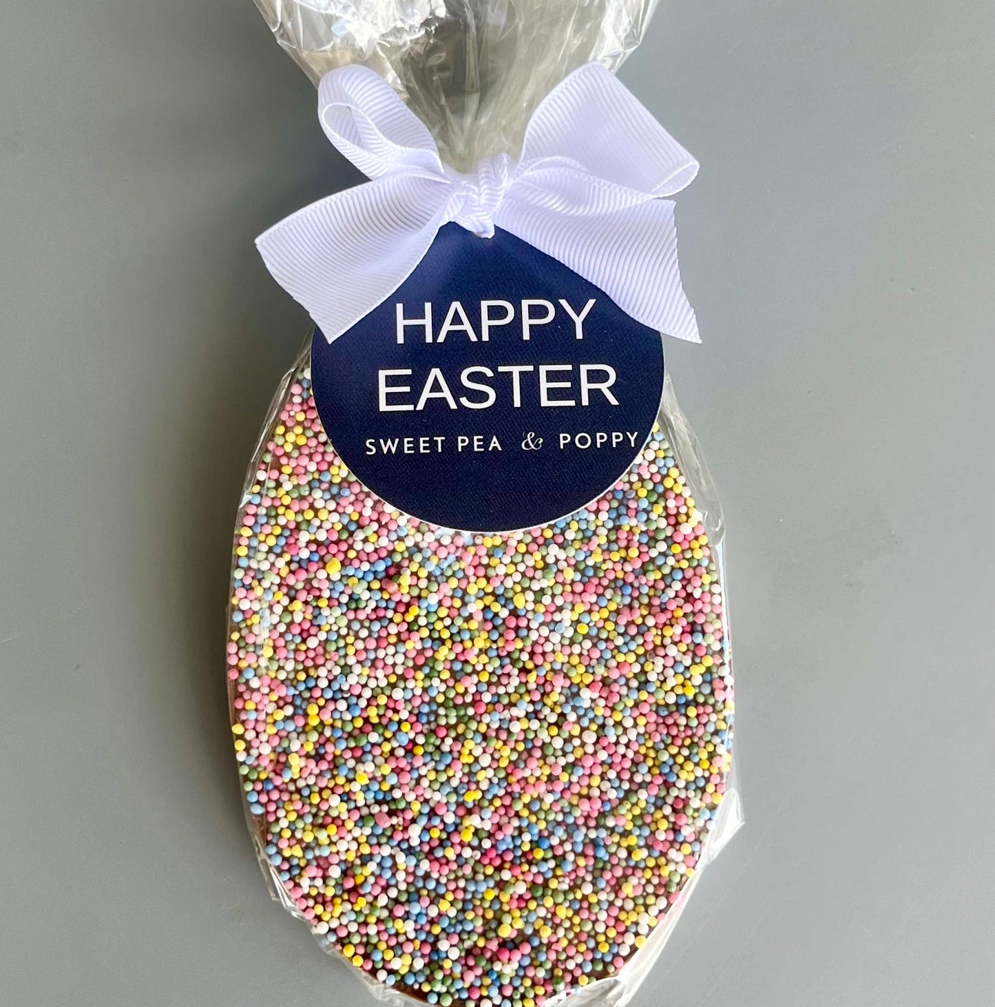 Easter egg-shaped chocolate bar with colorful sprinkles and 'Happy Easter' label on a grey background