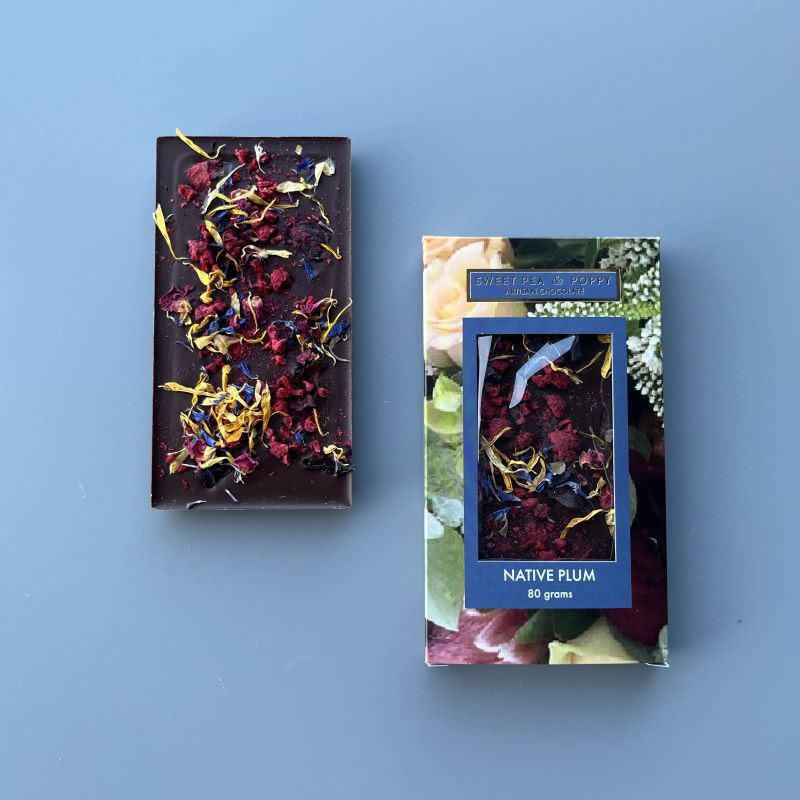 An unpackaged Native Plum dark chocolate bar with native plum and raspberry, sitting on top of a Sweet Pea & Poppy Native Plum packaged chocolate bar
