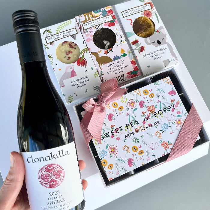 Bottle of Clonakilla wine with a box of assorted chocolates on a light gray background