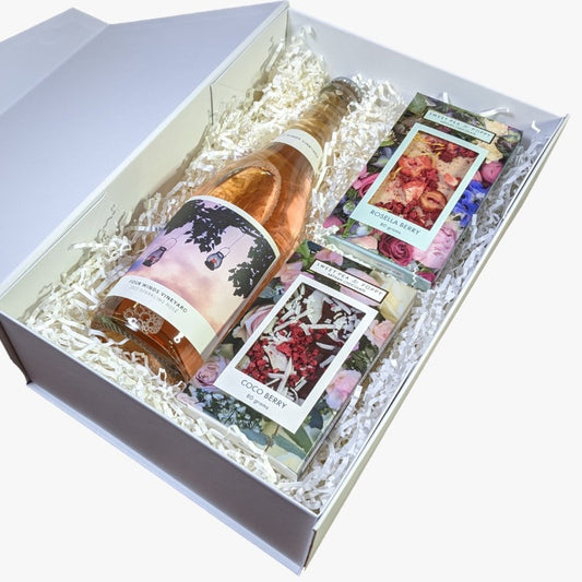 A gift hamper with sparkling rosé wine, a dark chocolate coco berry bar and a white chocolate rosella chocolate bar, presented in a white box with the lid open.
