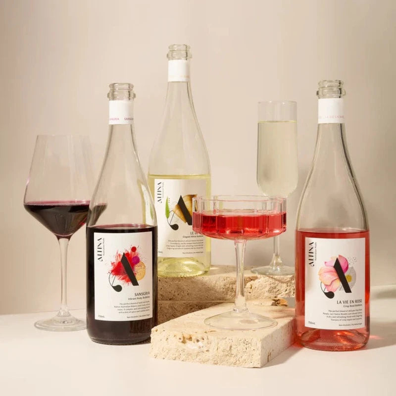 Three bottles of Altina non alcoholic wine with three glasses containing the wines, sitting ona styling brick prop