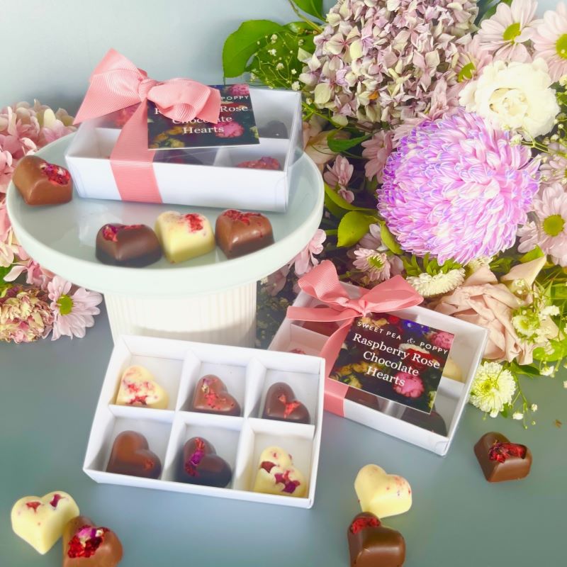 Three gift boxes of handmade chocolate hearts with a fresh floral bouquet background