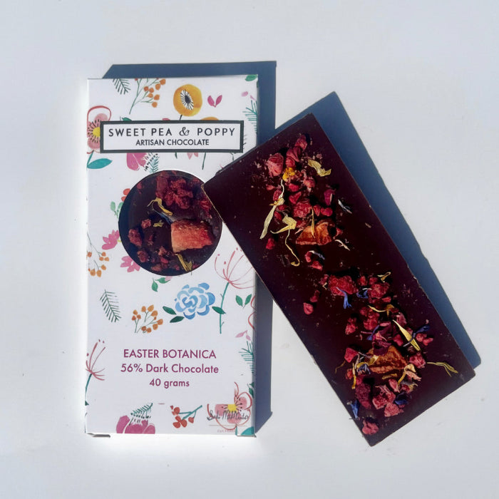 Dark chocolate bar with botanical elements next to its packaging on a white background 
