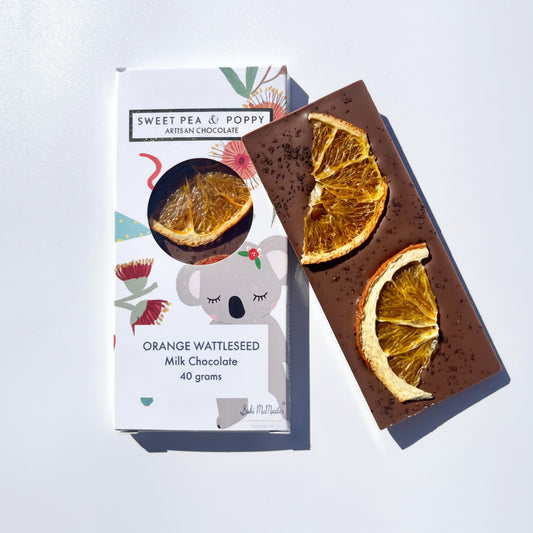 Chocolate bar with orange wattleseed flavor next to its packaging on a light gray background