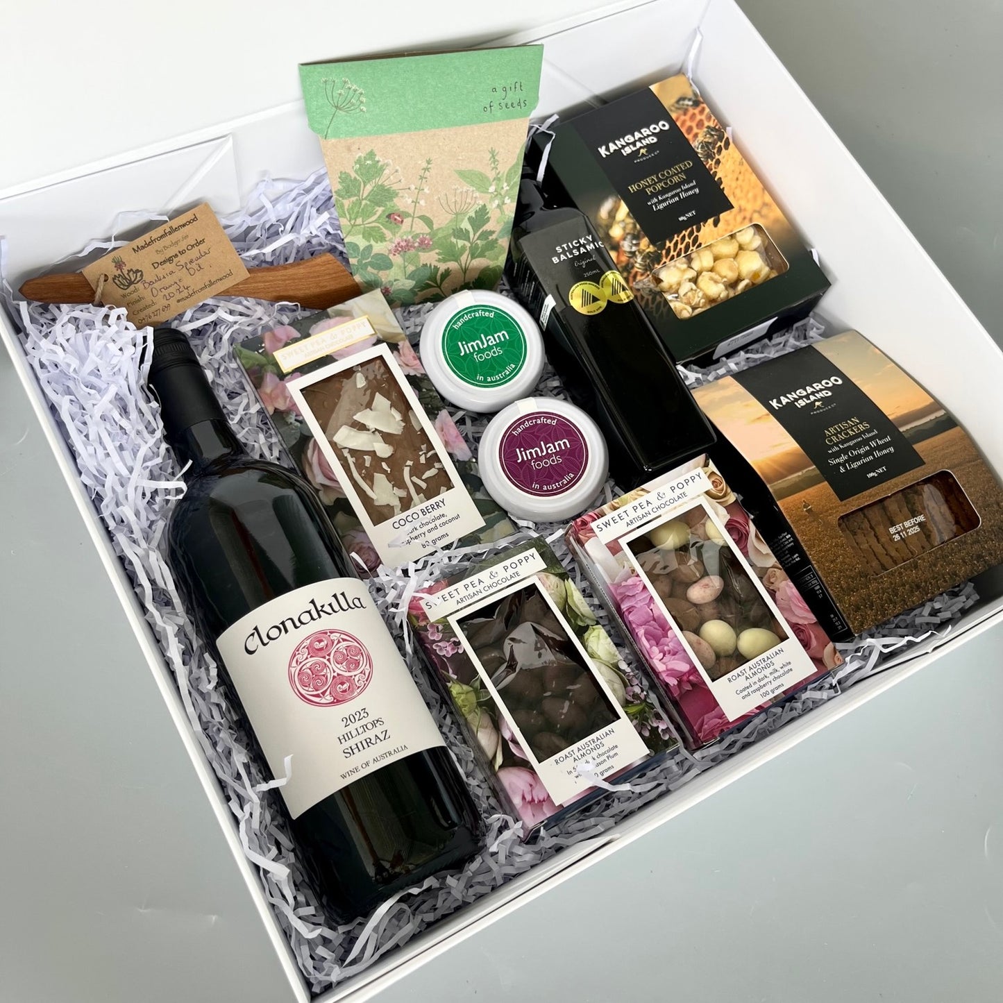 A gift hamper with wine, chocolate, wooden server, gourmet pastes, balsamic vinegar, crackers, popcorn and a gift of seeds 