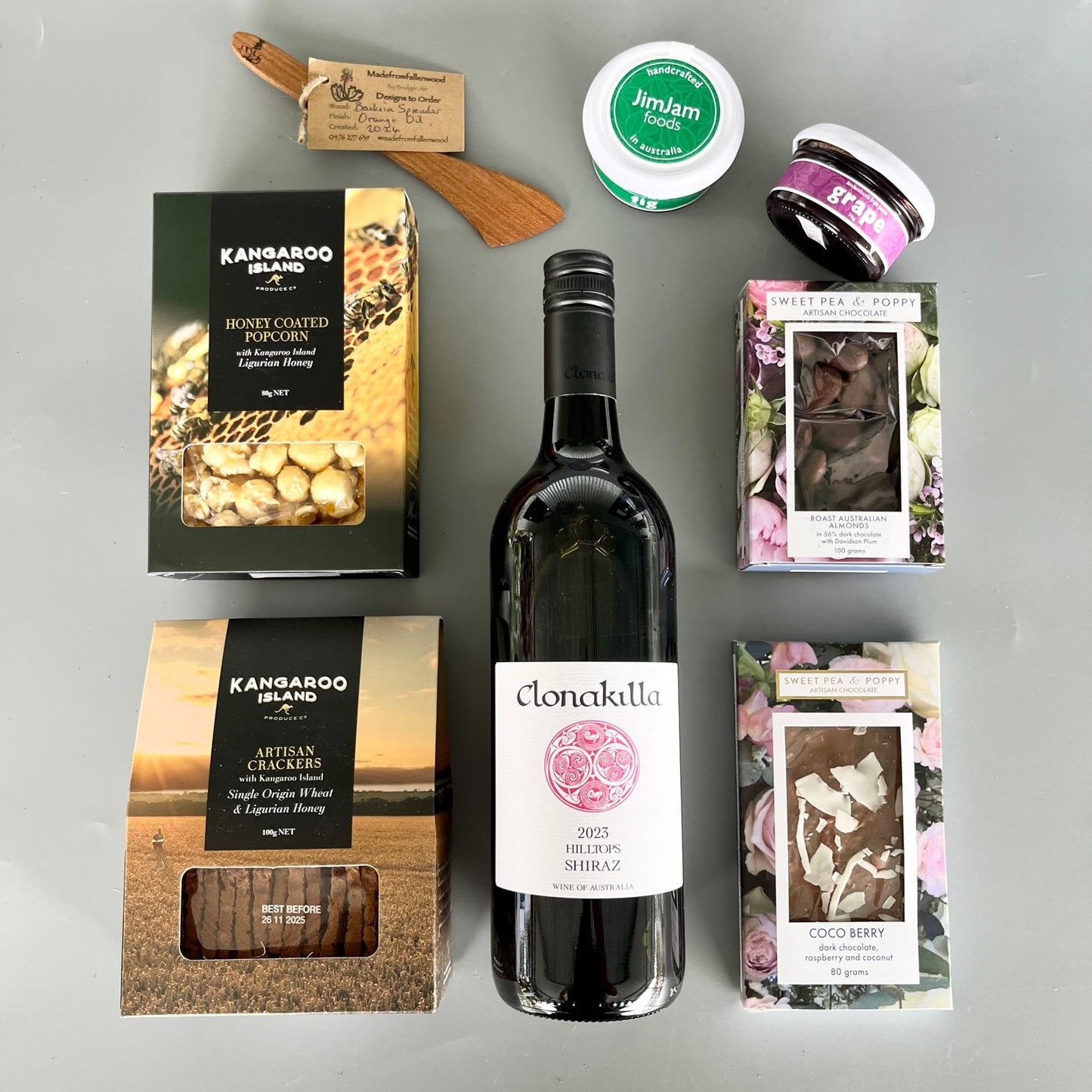 A flatlay gift hamper with wine, chocolate, wooden server, gourmet pastes, crackers and popcorn 