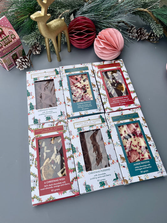 Packaged chocolate bars with Christmas-themed design on a gray surface with decorative items.