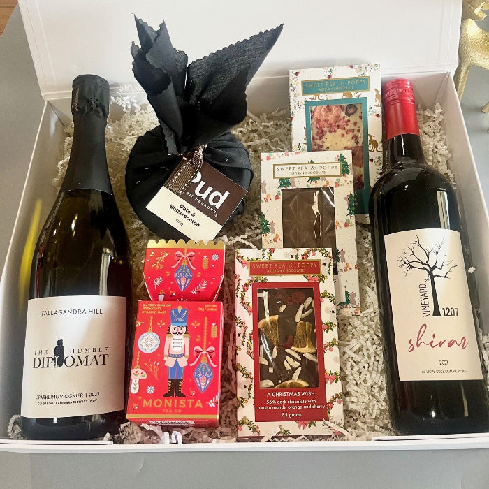 A gourmet gift basket with two bottles of wine, three Sweet Pea & Poppy Christmas chocolate bars, a Christmas pudding and a festive Christmas tea