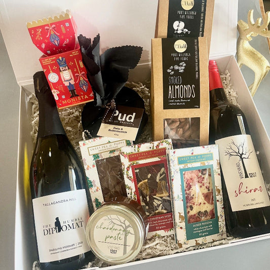 A big gift basket with two bottles of wine, three artisan chocolate bars, a Christmas pudding, a jar of chardonnay paste, a Christmas tea and two boxes of gourmet almonds and toffee 