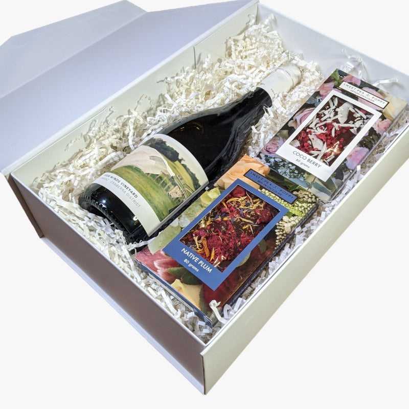 A gift hamper with red wine, a dark chocolate coco berry bar and a dark chocolate native plum chocolate bar, presented in a white box with the lid open. 