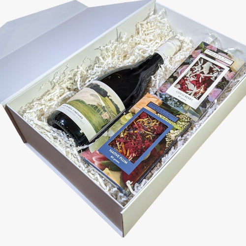 A gift hamper with red wine, a dark chocolate coco berry bar and a dark chocolate native plum chocolate bar, presented in a white box with the lid open. 