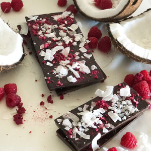 A pile of dark chocolate, raspberry and coconut Berry chocolate bars with coconut and raspberry decorations