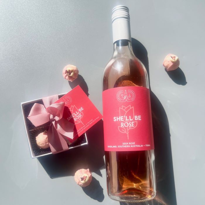 A gift box of handmade chocolate truffles with a pink bow, next to a bottle of rose wine