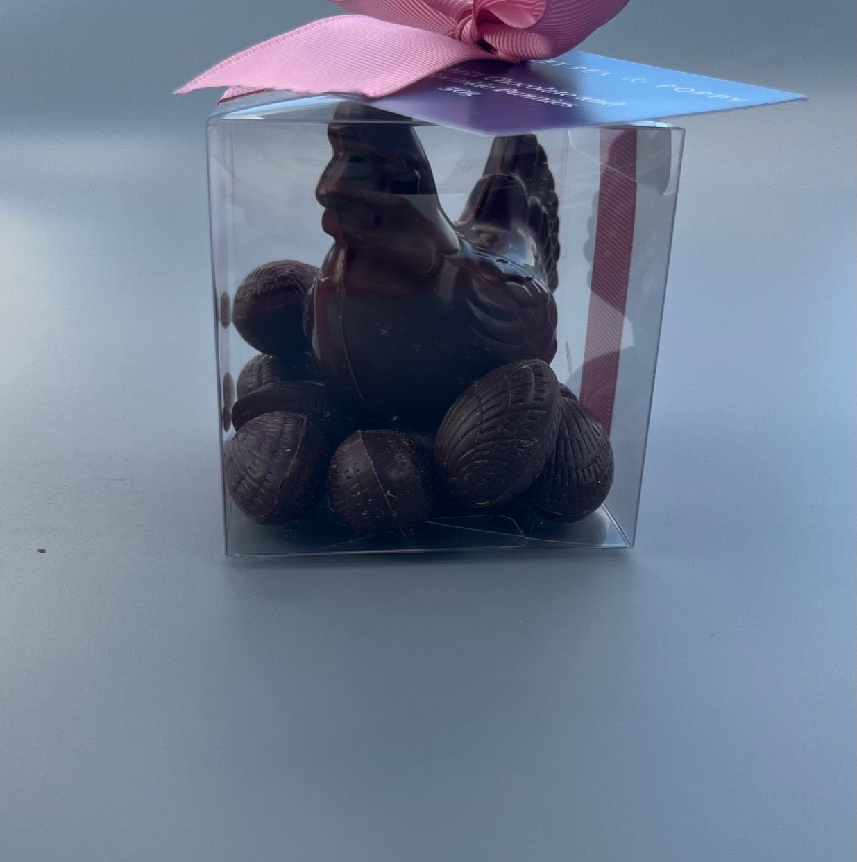 A gift box with a dark chocolate hen sitting on solid dark chocolate Easter eggs