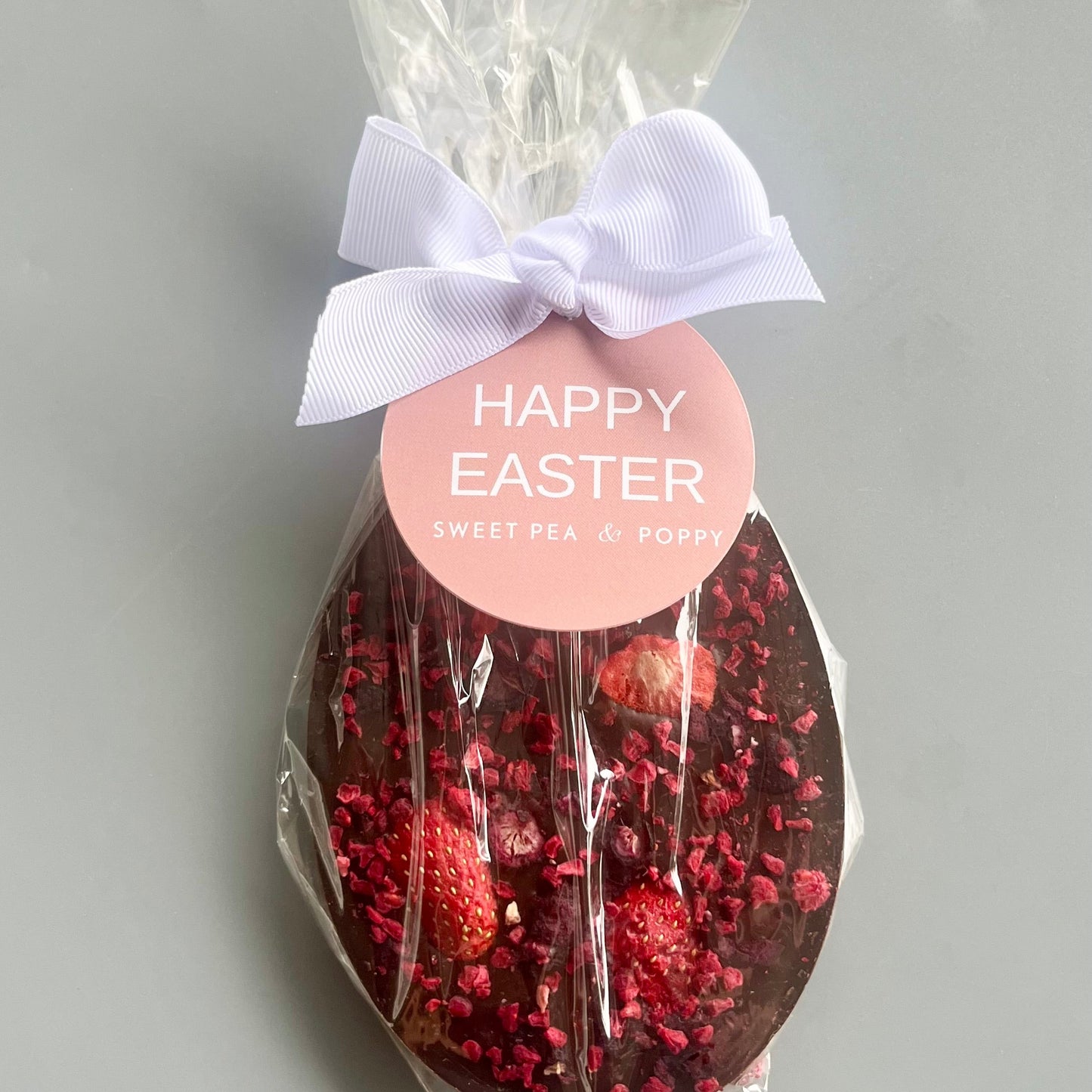 Chocolate Easter egg with berries and a 'Happy Easter' label on a grey background