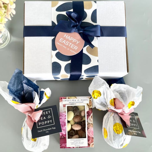 A Happy Easter gift hamper, Sweet Pea & Poppy chocolate eggs, and chocolate coated Australian almonds on a grey surface.