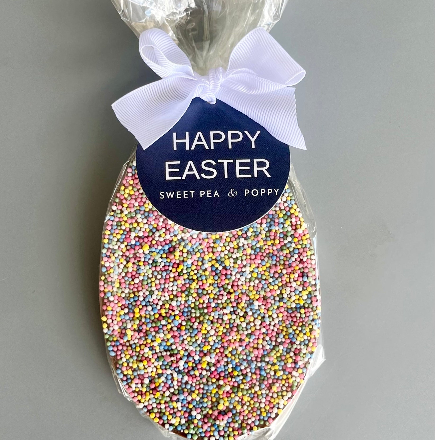 Easter egg-shaped chocolate bar with colorful sprinkles and 'Happy Easter' label on a grey background