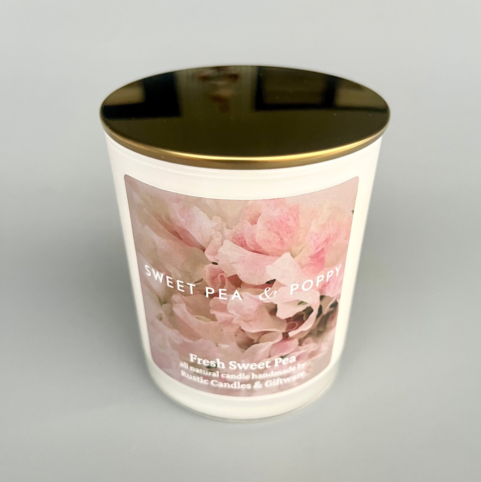 Candle with floral design and gold lid on a grey background