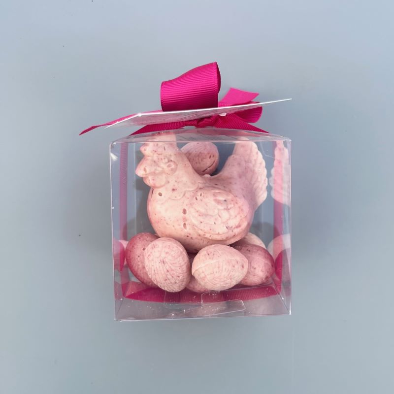 A gift box with a raspberry white chocolate hen sitting on solid raspberry white chocolate Easter eggs