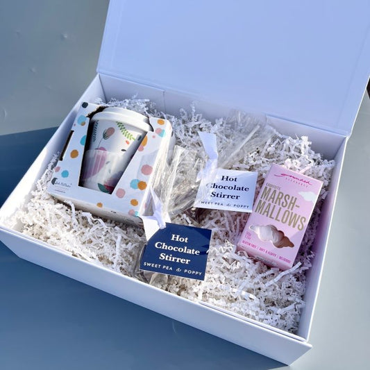 A gift hamper box with a keep cup, two hot chocolate stirrers and a box of marshmallows