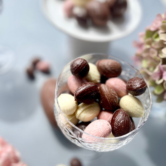 Glass bowl filled with assorted chocolate Easter eggs on a grey and floral background