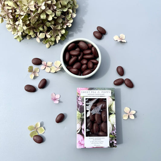 A box of dark chocolate coated Australian almonds with a bowl of the chocolate coated almonds