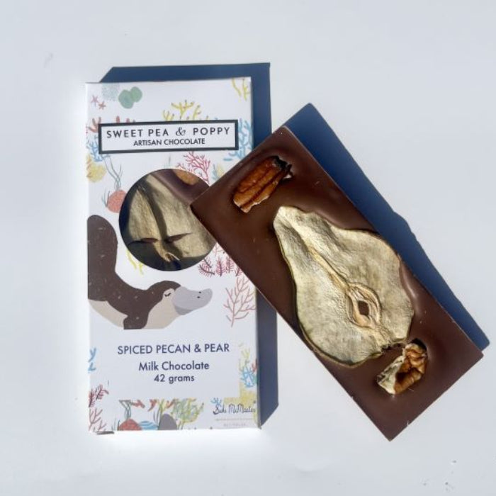 Chocolate bar with pecans and pear next to its packaging on a white background