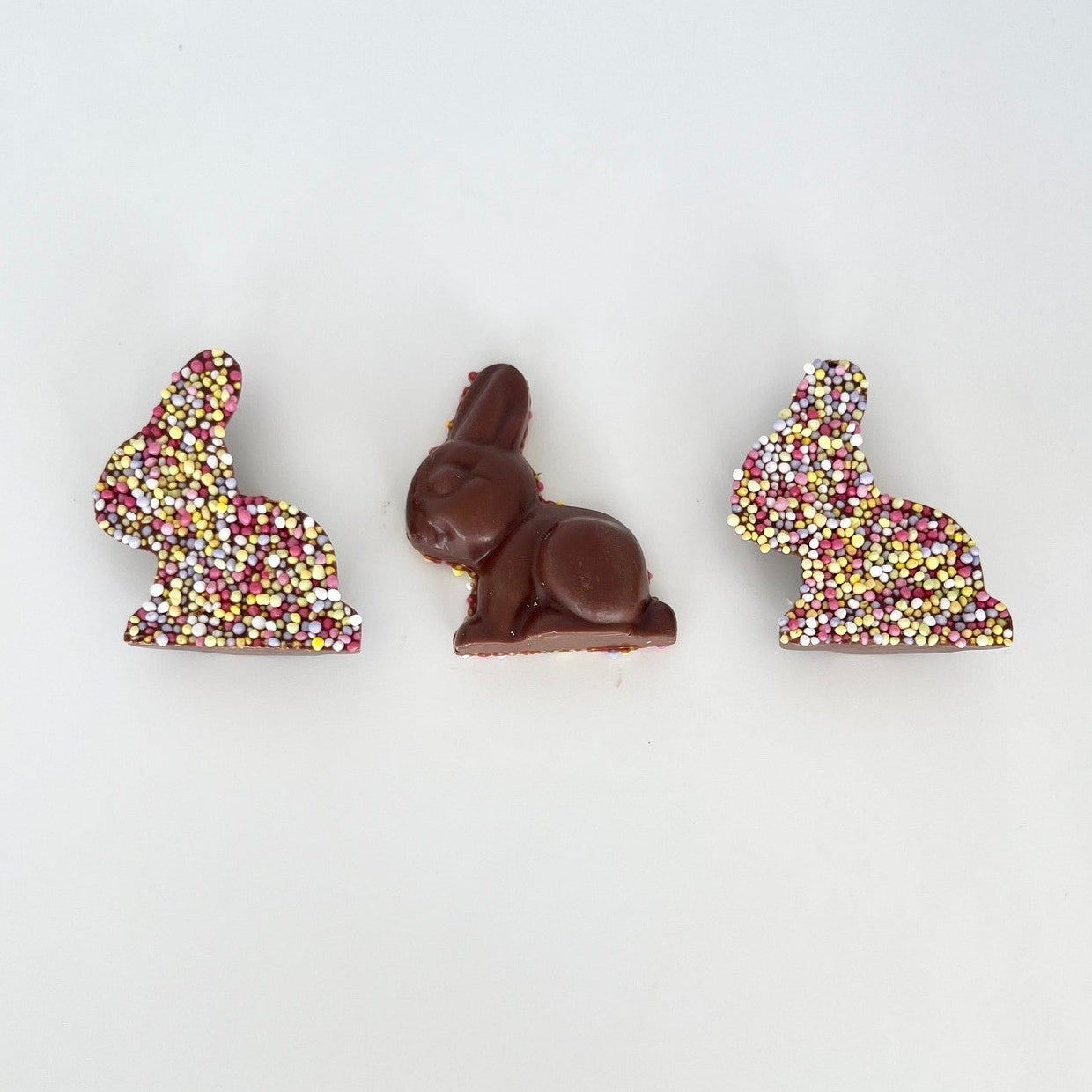 Three milk chocolate Easter bunnies with sprinkles on a white background