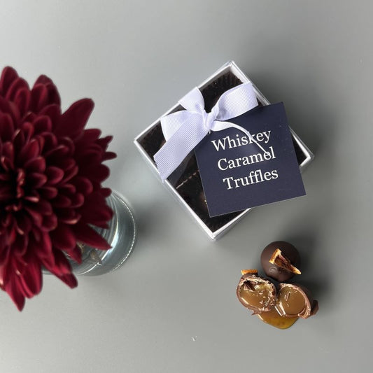 A gift box of Sweet Pea & Poppy Whiskey Caramel gourmet chocolate truffles  with whiskey caramel chocolate truffles featuring gooey caramel in the foreground