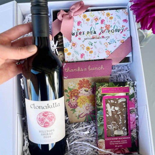 Gift box with Clonakilty wine bottle, chocolate, cards, and other items on a light background