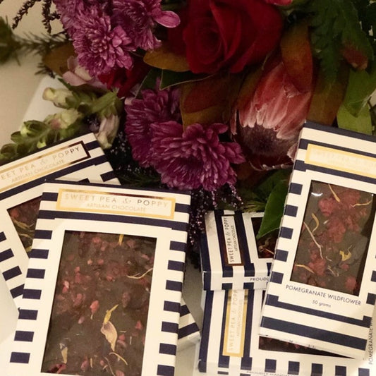 A pile of dark chocolate bars in blue and white stripe boxes with some flowers in the background